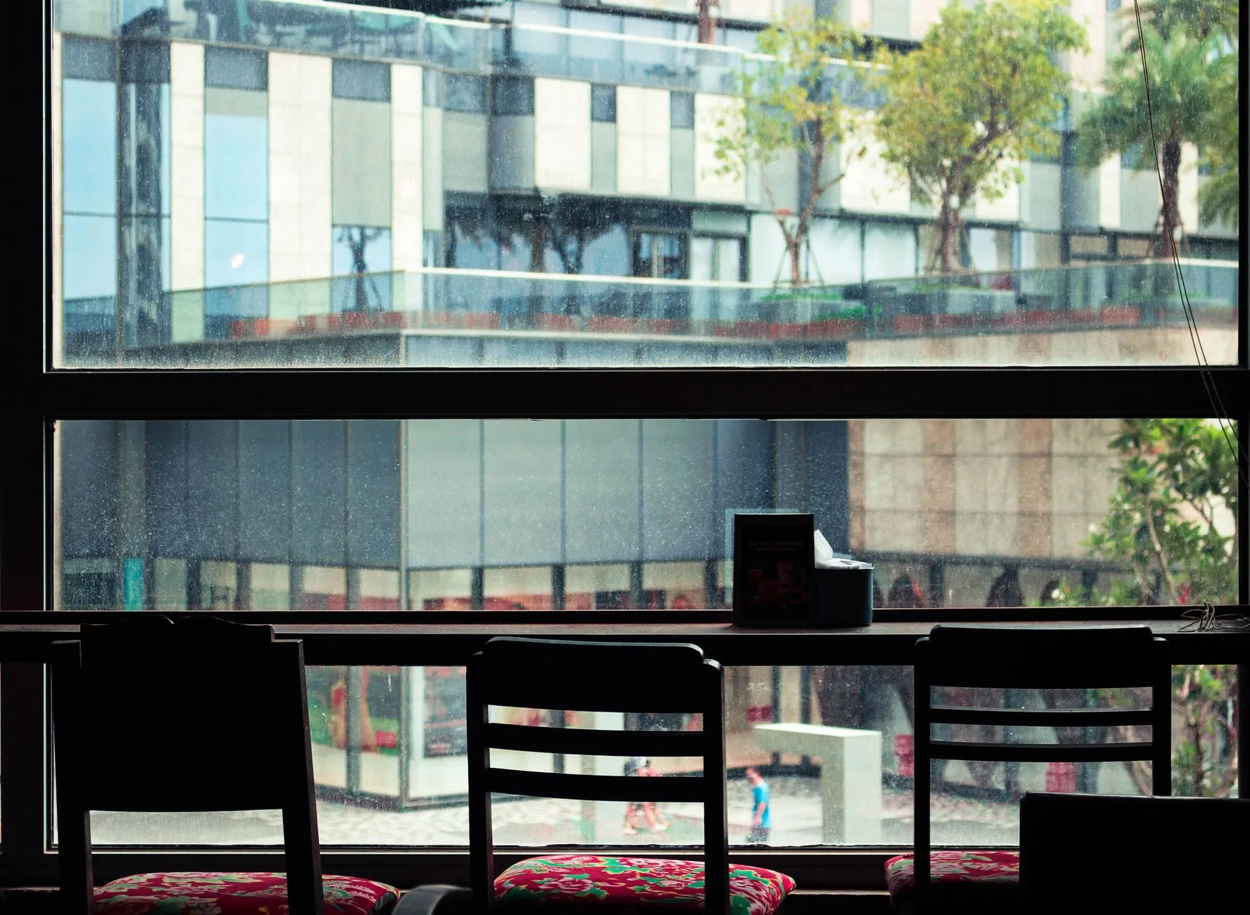 An empty wooden chair beside a large café window looking onto a city.