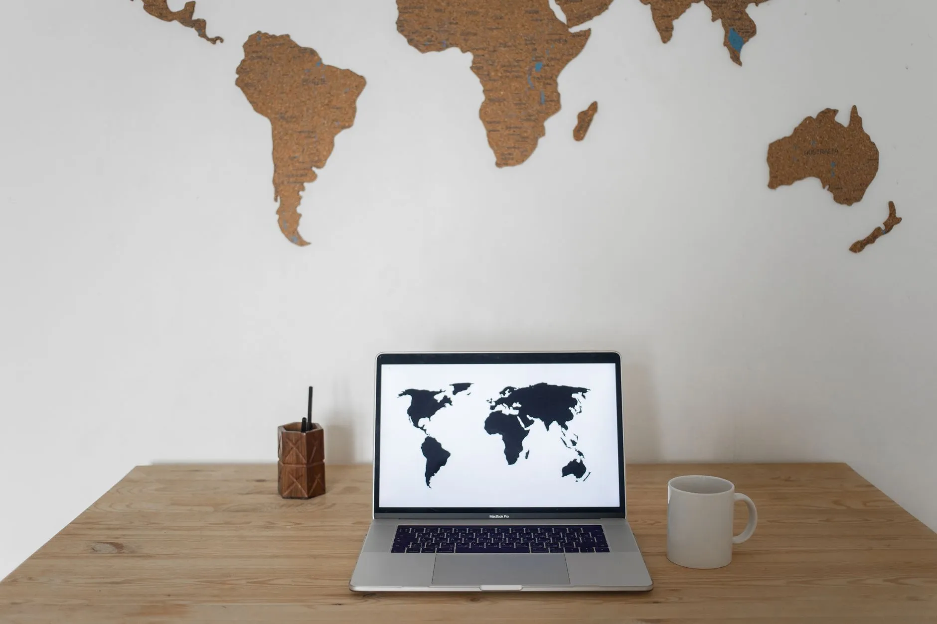 A world map on a wall behind a desk with a laptop, cup, and pen holder.