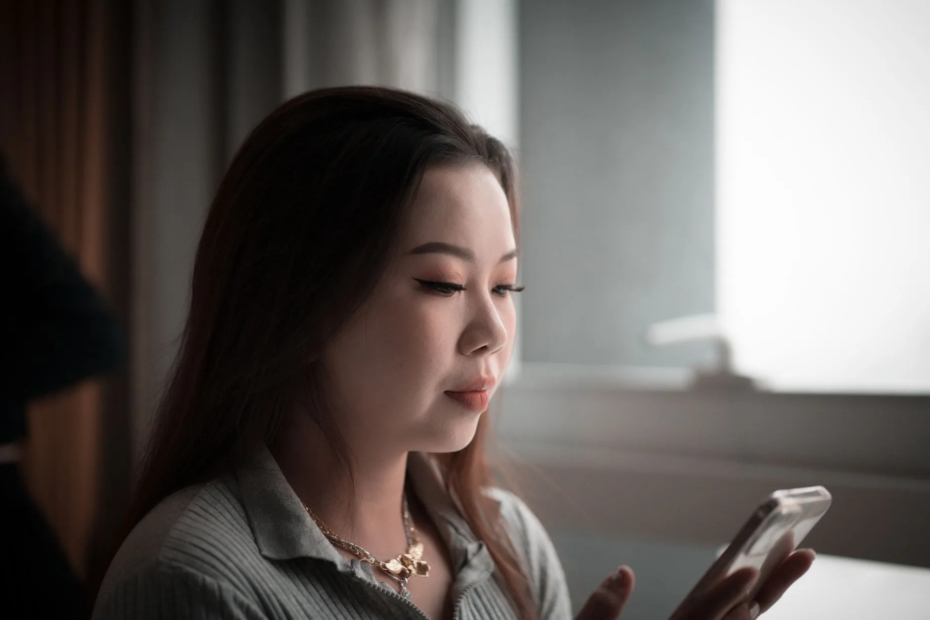 An Asian woman concentrating on her smartphone in a softly lit room.