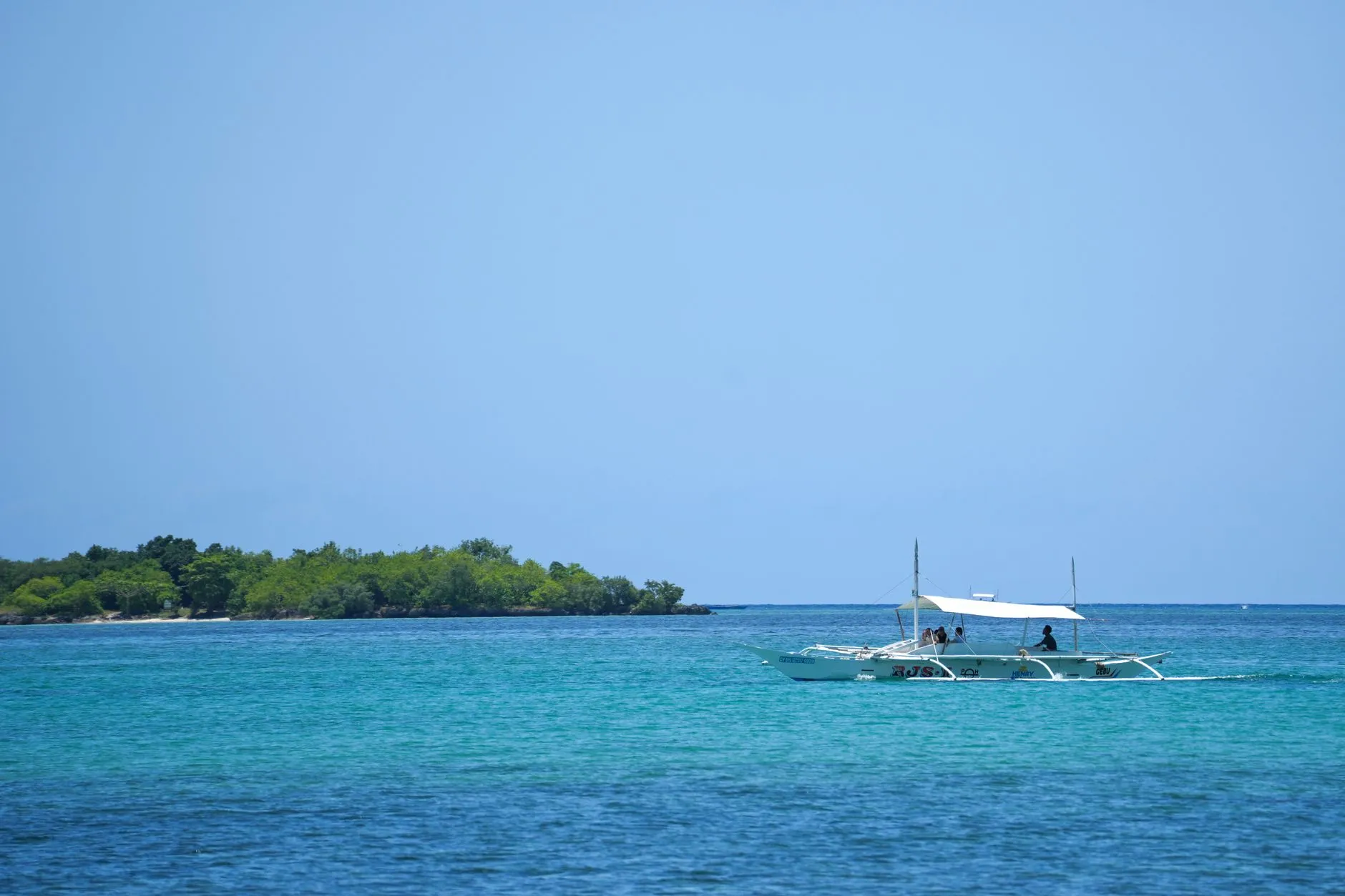 A traditional outrigger boat on blue water near green islands in the Philippines.