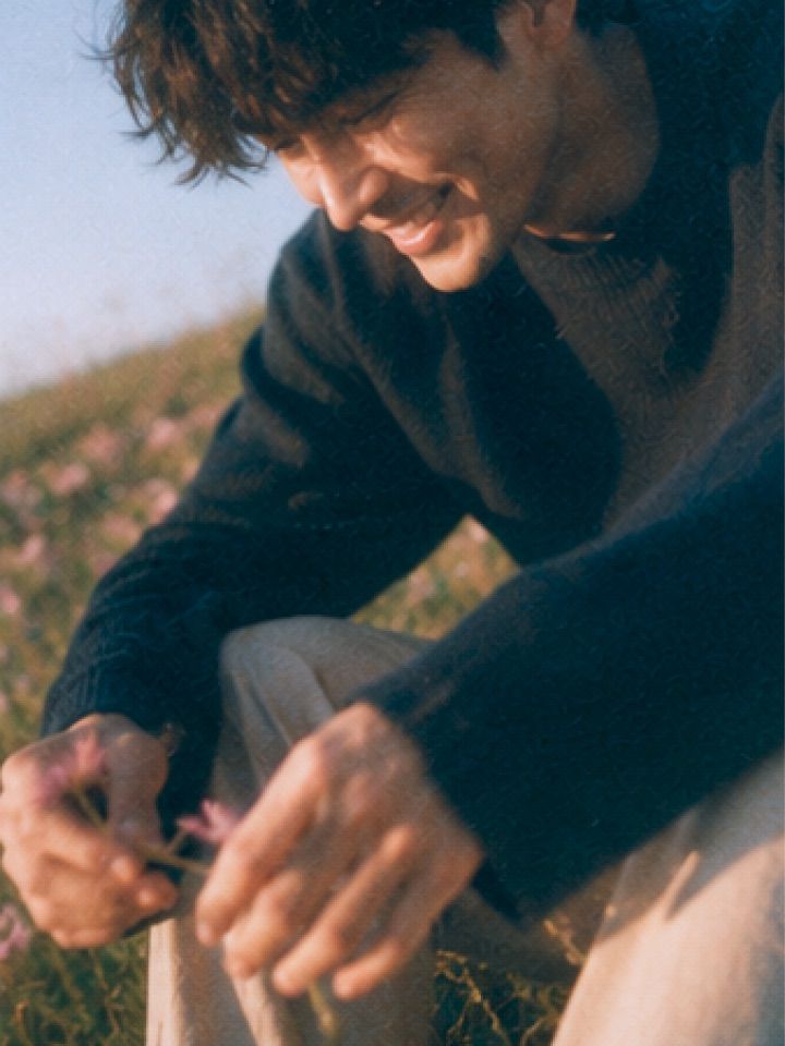 A man smiling among wildflowers in a sunlit field