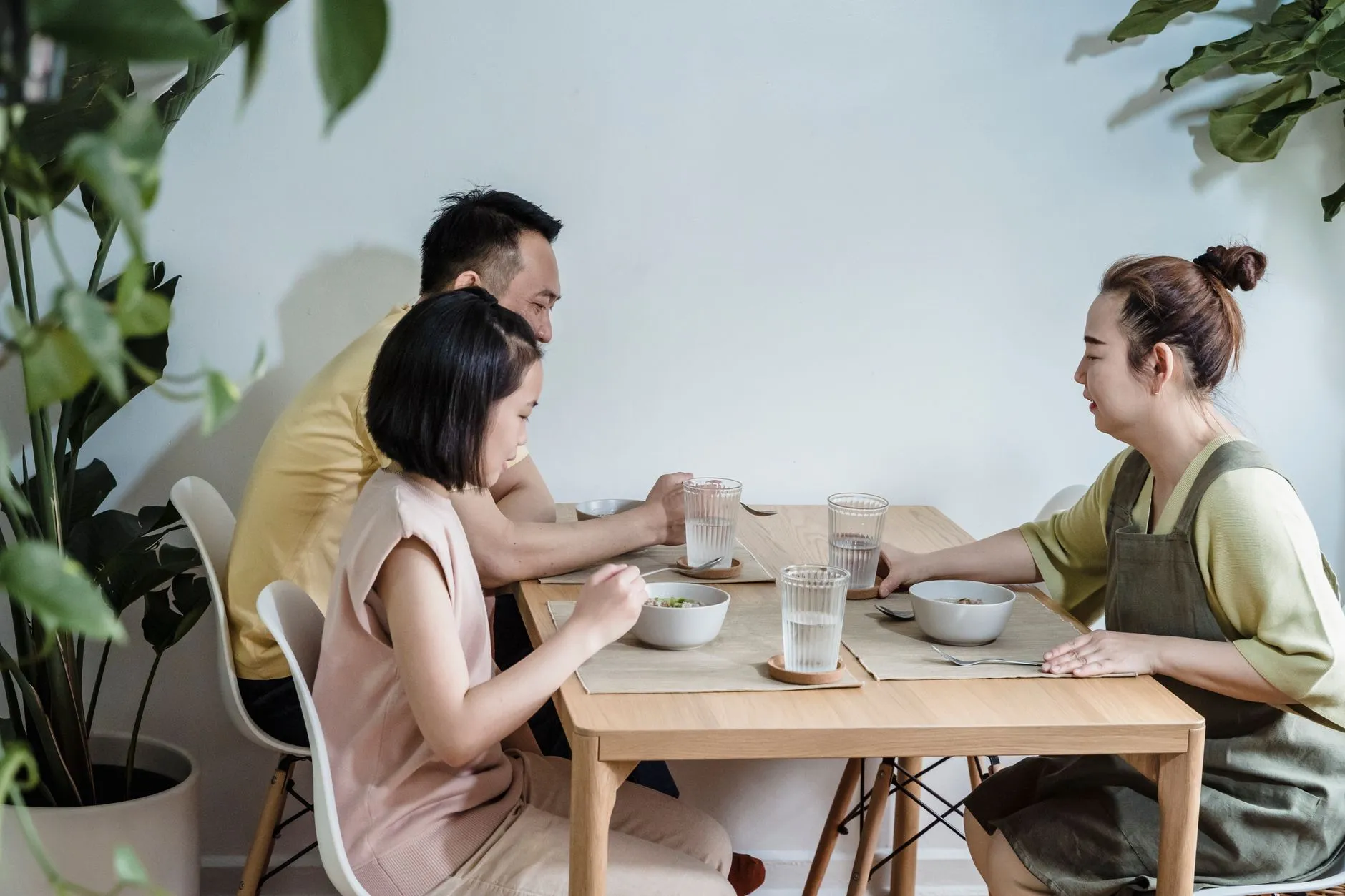A family sharing a meal together at a wooden table surrounded by houseplants.