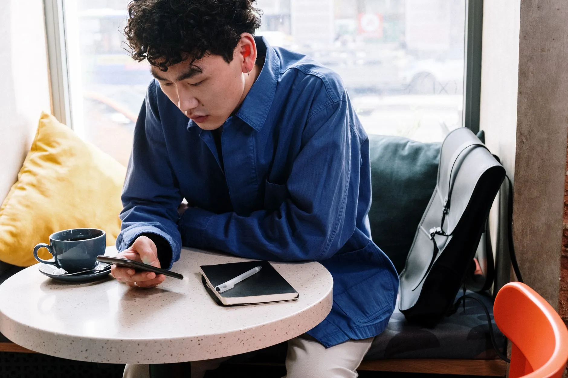 A young Asian man using his smartphone at a café table.